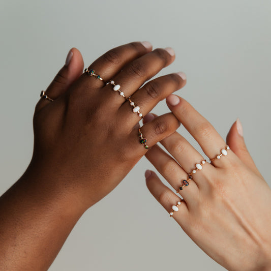 Two hands wearing oval triple gemstone rings with white opals set in gold