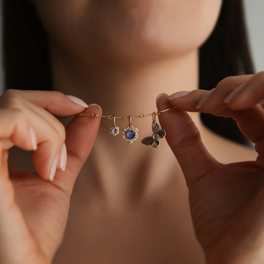 A person holding up three charms, two flowers and a butterfly, which are dangling from a gold chain.