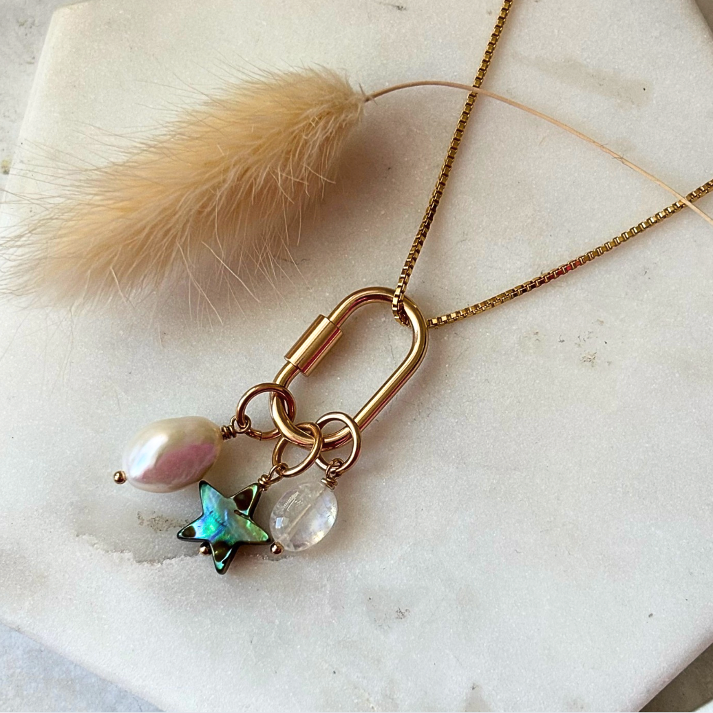 Necklace with gold clasp, pearl, and butterfly charm on a marble surface.