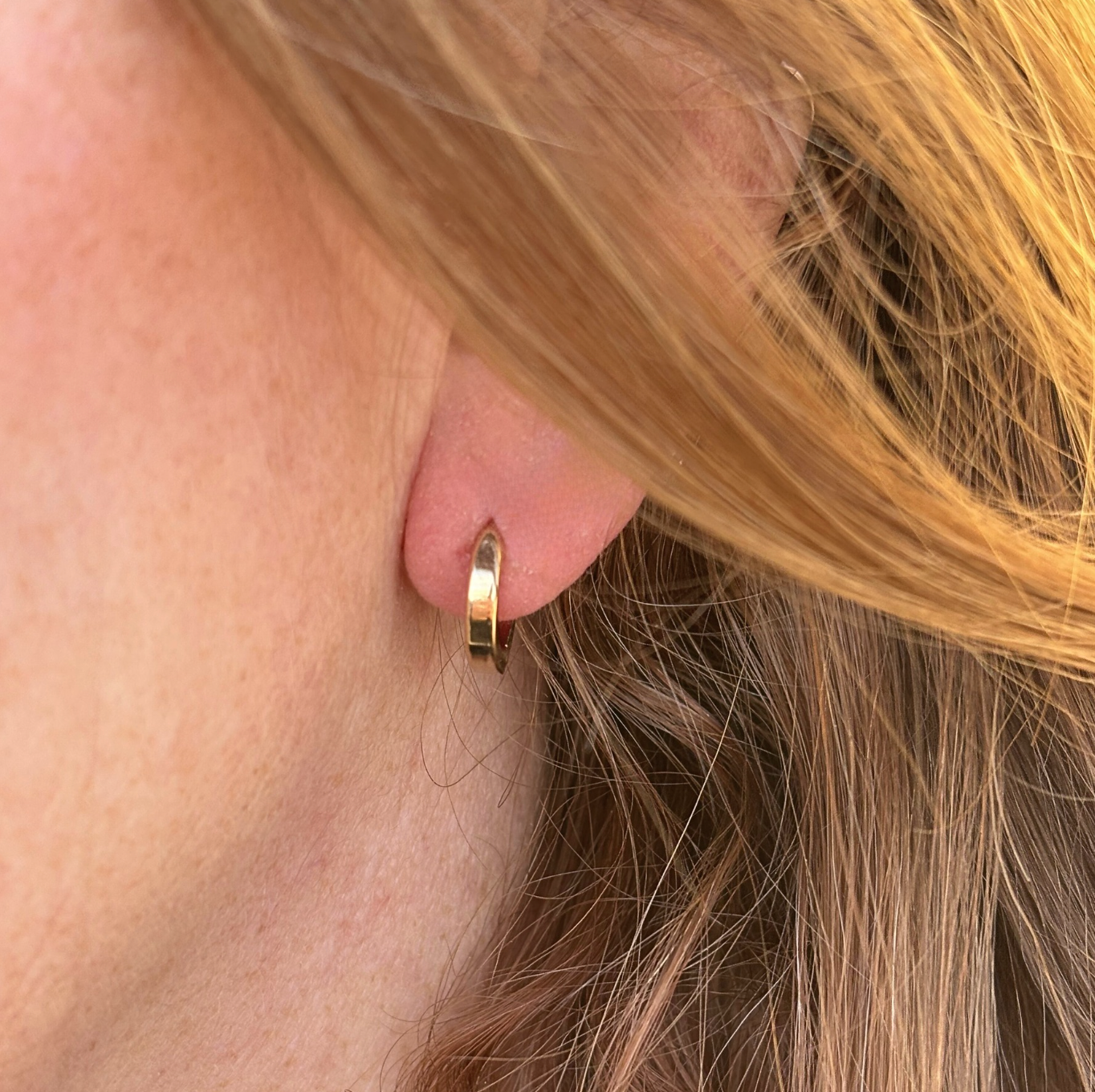Close-up of a person wearing a gold hoop earring with blonde hair.