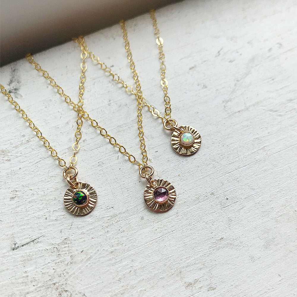 Three Aura birthstone necklaces with mini gold-filled or sterling silver discs and gemstones, displayed on a light background.