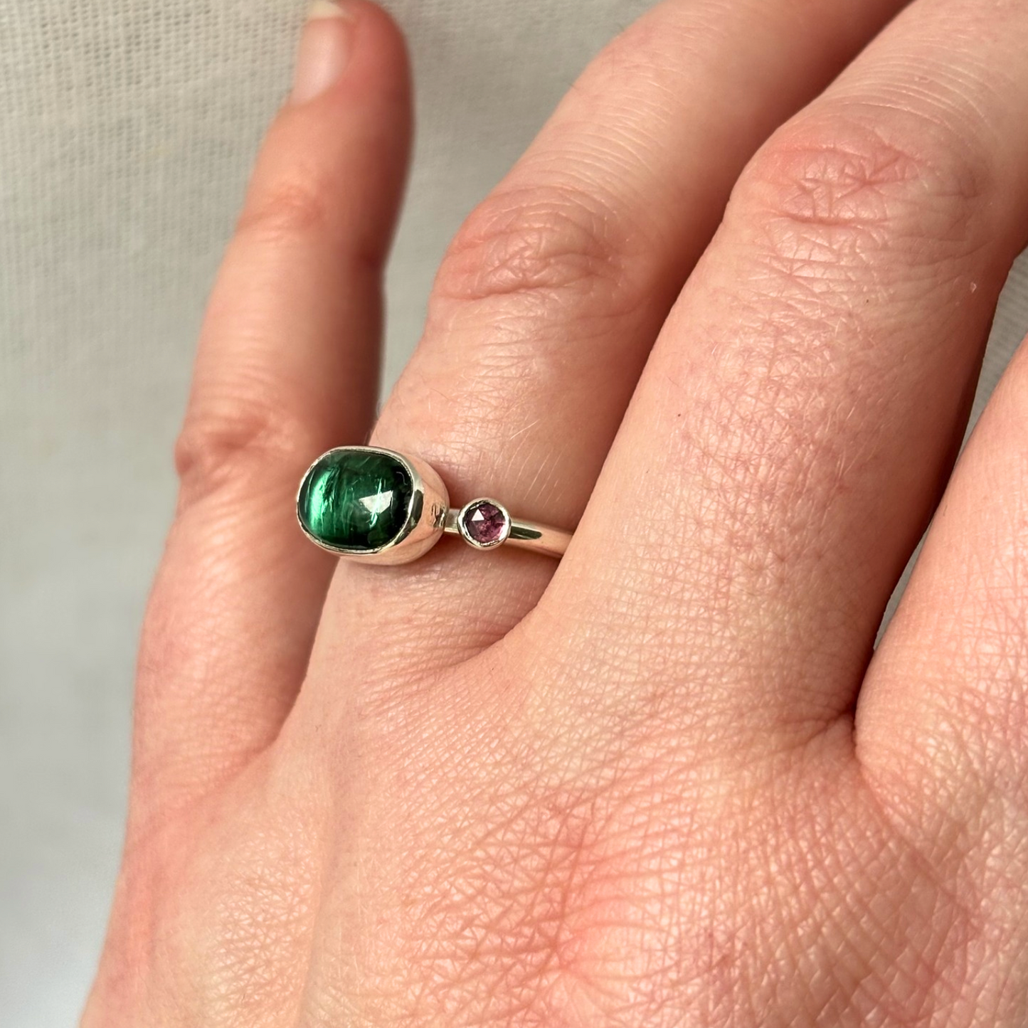 Ring with a green gemstone on a finger against a neutral background