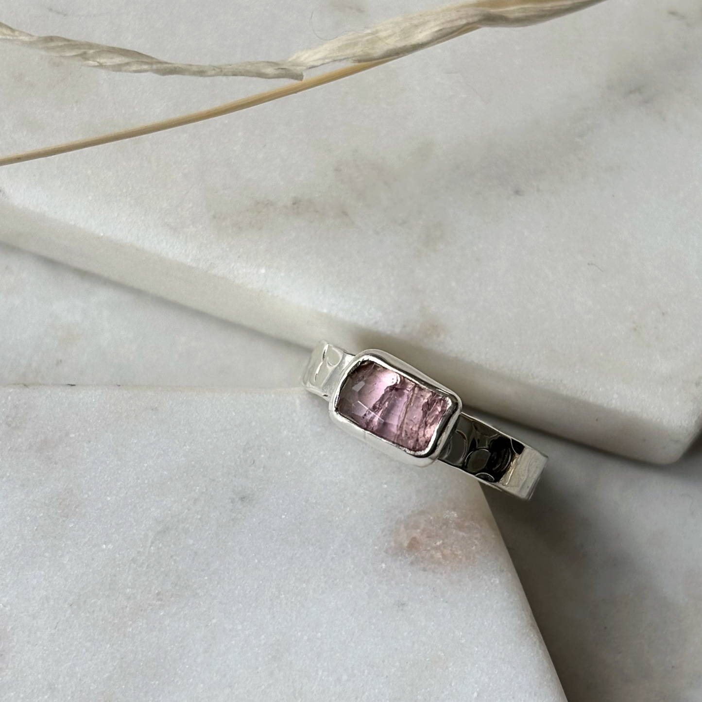 Silver ring with a pink gemstone on a marble surface