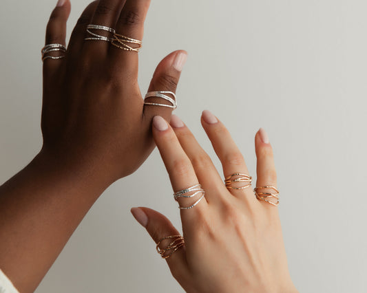 Two hands with multiple gold rings on a neutral background