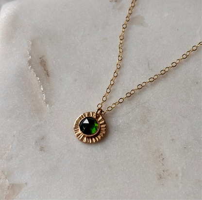 A green gemstone pendant necklace on a marble background, set in gold.