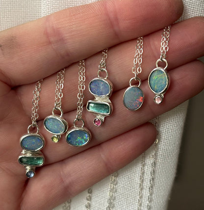 Hand holding multiple silver necklaces with gemstone pendants against a neutral background