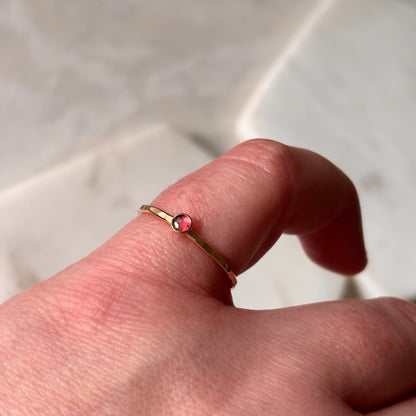 Gold ring with a pink gemstone on a finger against a neutral background
