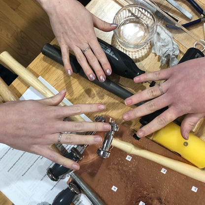 Three people's hands showing the rings they made with tools in the background.