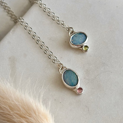 Two silver necklaces with gemstone pendants on a light background