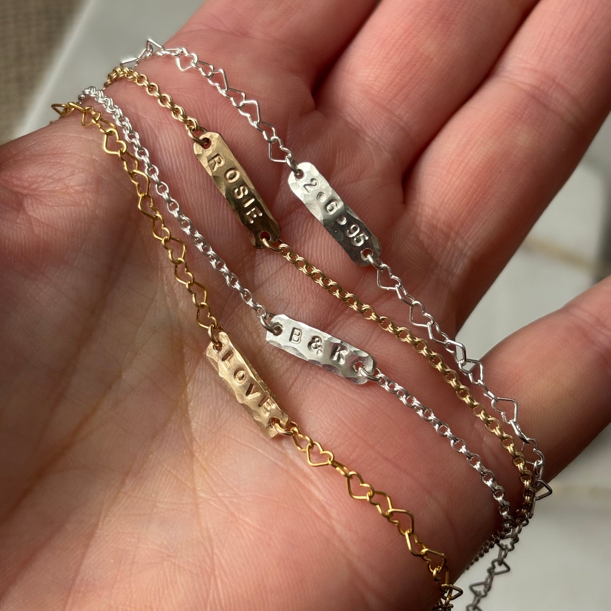 Three gold and silver chains with engraved names on a hand.