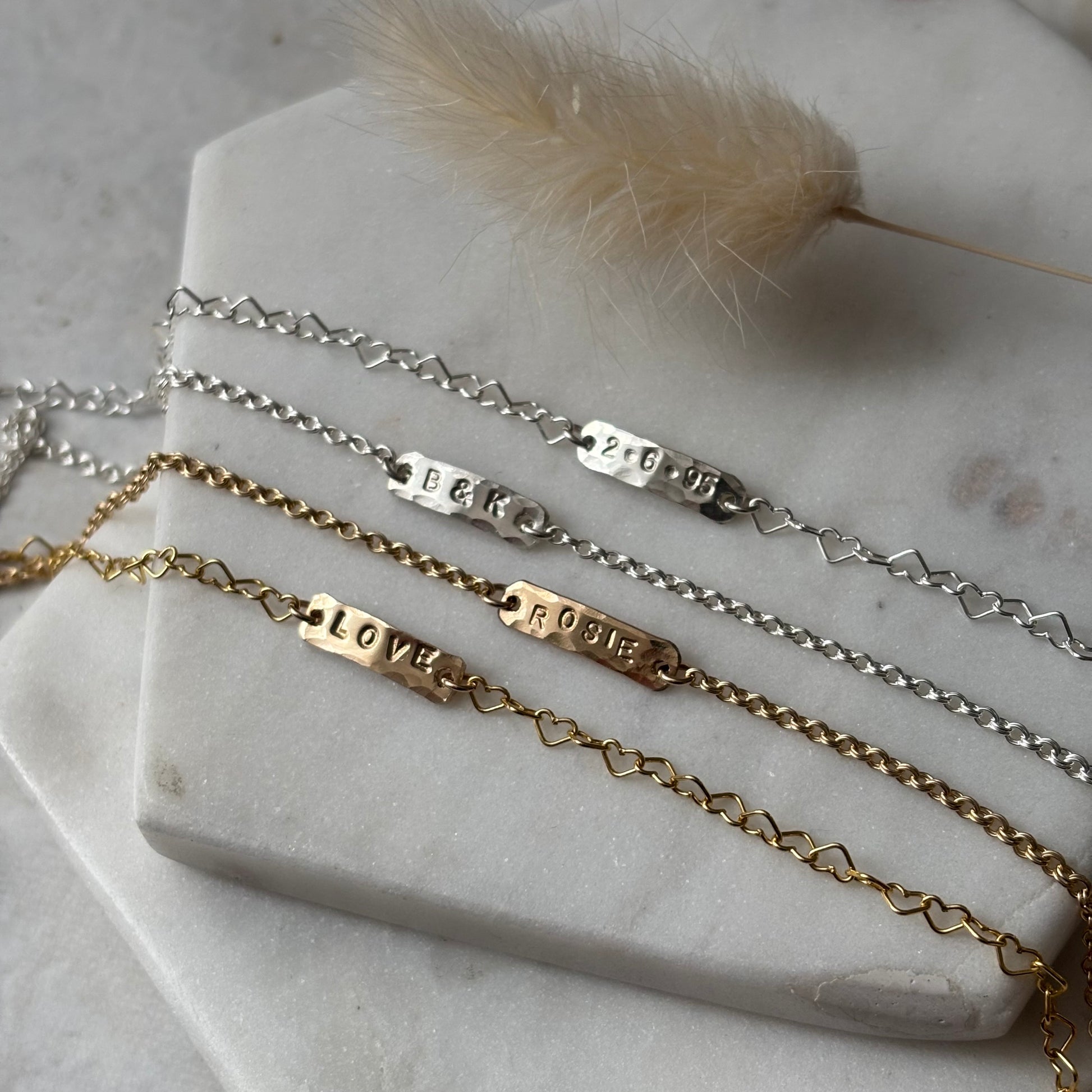 Three gold and silver bracelets with engraved names on a marble surface.