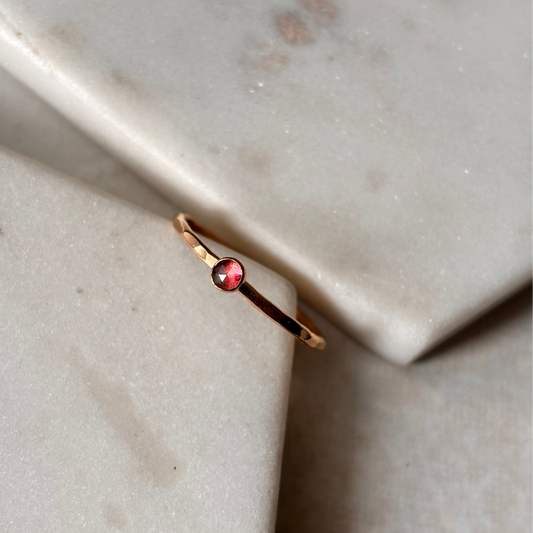 Gold ring with a red gemstone on a marble surface