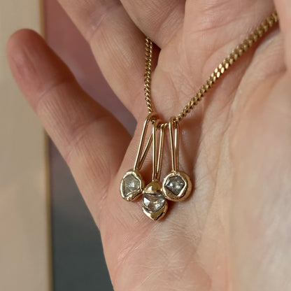 Gold necklace with three diamond pendants on a hand against a neutral background