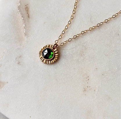 A gold-fill or sterling silver necklace with a pendant featuring a rose-cut green emerald, displayed against a marble background.