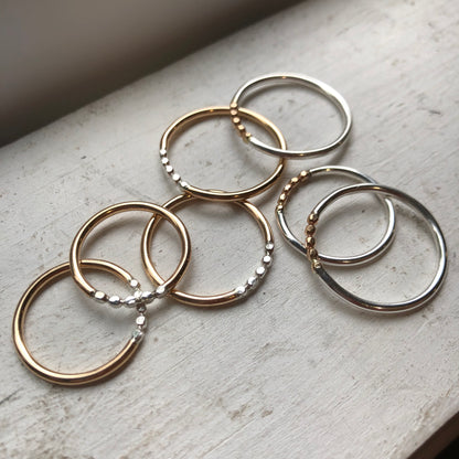 Rings with a gold band and silver orb accents and another with a silver band and gold orb accents, placed on a marble surface.