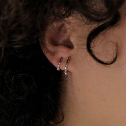 A set of two J-hoop earrings made of sterling silver with hand-textured orbs, worn in an ear.
