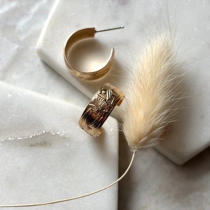 Gold floral hoop earring on a marble surface with a dried flower.