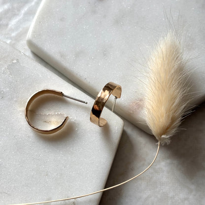 Gold hoop earrings on a marble surface with a feather