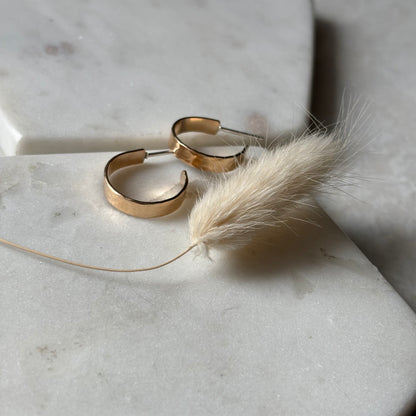 Gold hoop earrings with a dried pampas grass on a marble surface