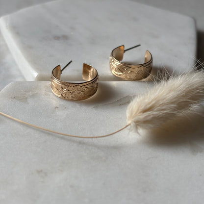 Gold hoop earrings on a marble surface with a dried plant