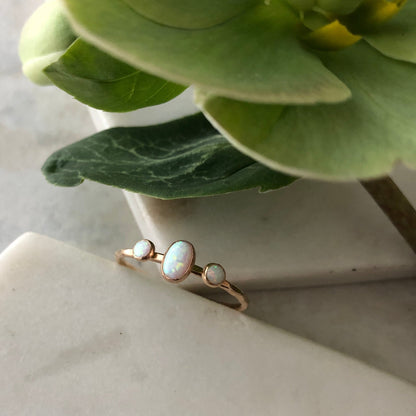 An oval triple gemstone ring with white opal set in gold, displayed on a marble surface.