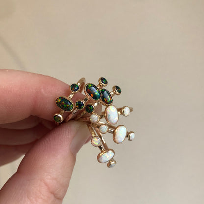 Multiple oval triple gemstone rings with black opal set in gold displayed on a white surface.