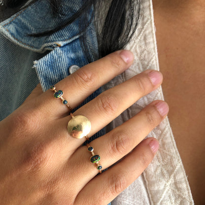 A hand wearing oval triple gemstone rings with black opal set in gold.