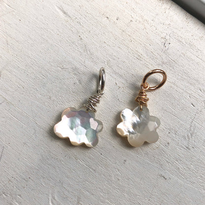 Two Mother of Pearl cloud charms, one with a silver hoop and the other with a gold-filled hoop, placed on a textured grey surface.