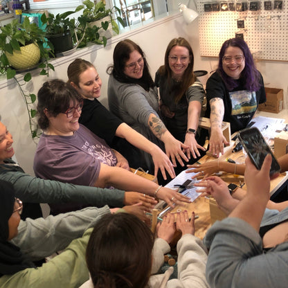 A group of people smiling and showing the rings they made in a jewellery making class.
