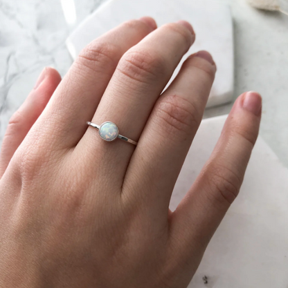 Hand wearing a silver ring with a central gemstone on a light background