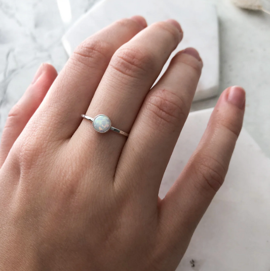 Hand wearing a silver ring with a central gemstone on a light background