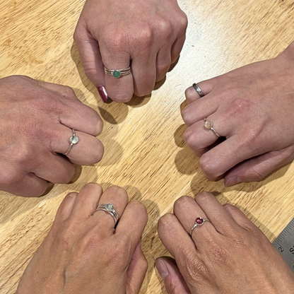 hands in a circle wearing gemstone rings