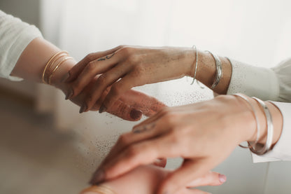 Three hands with jewelry held together against a light background