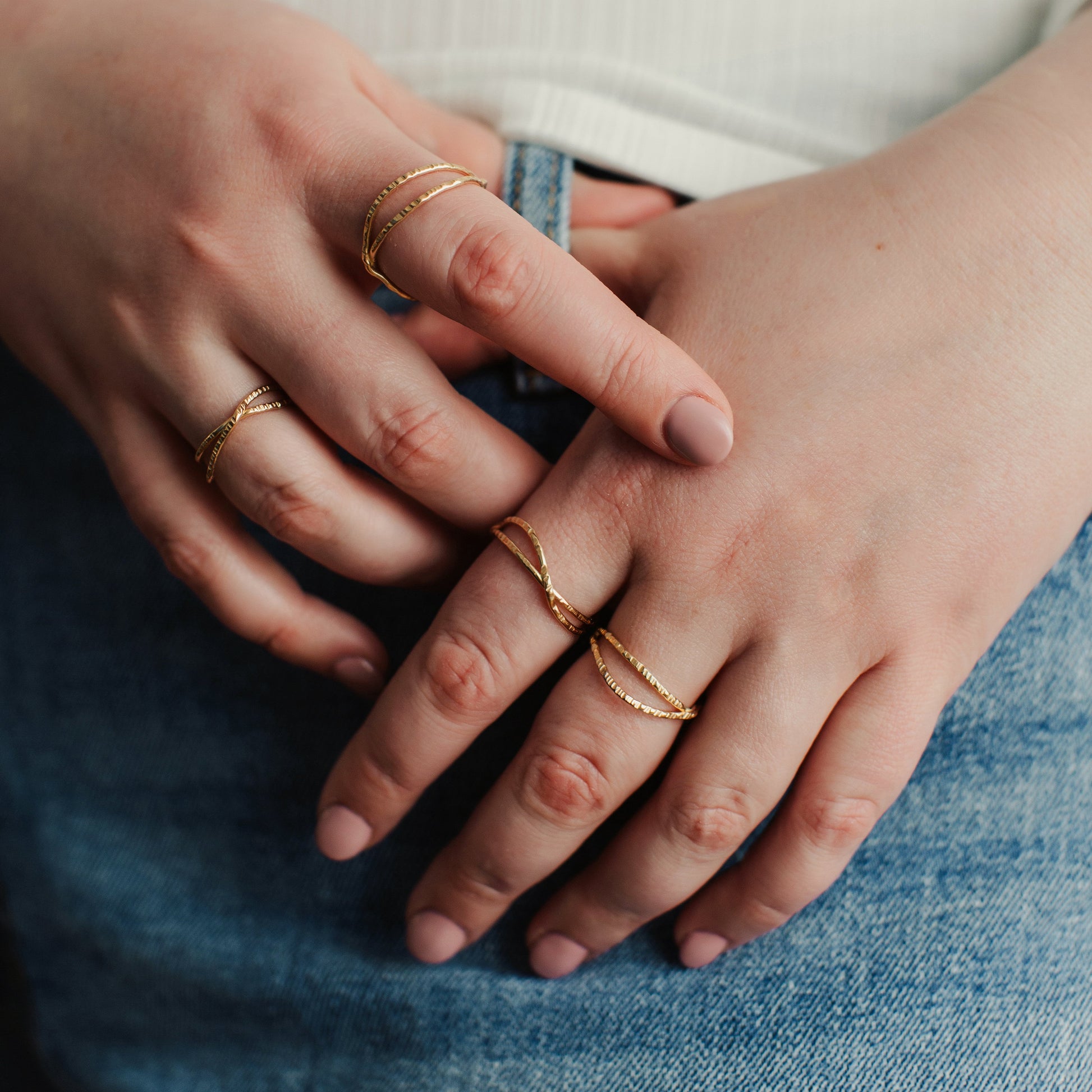 Close-up of hands with gold rings on fingers, wearing a white shirt and blue jeans.