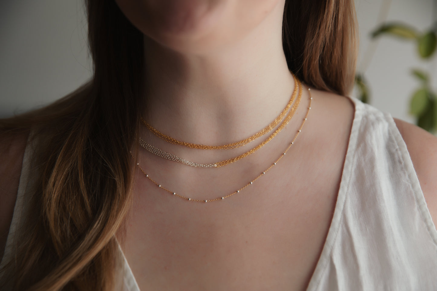 Close-up of a person wearing a delicate gold necklace with a blurred background