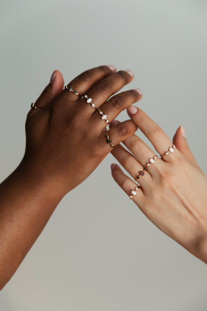Two hands wearing oval triple gemstone rings with white opals set in gold