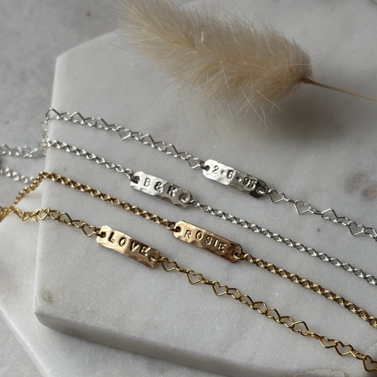 Gold and silver bracelets with engraved names on a marble surface.