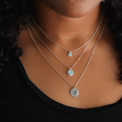 A person with brown skin wearing various sizes of silver pendants with blue aquamarine.