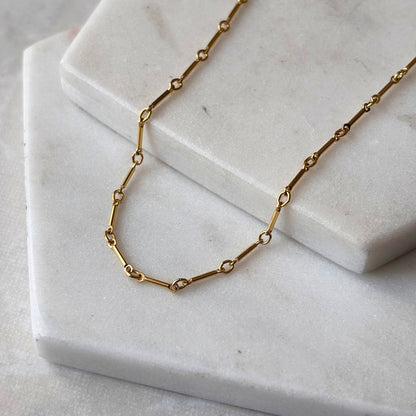 A gold bar link necklace draped on a marble background