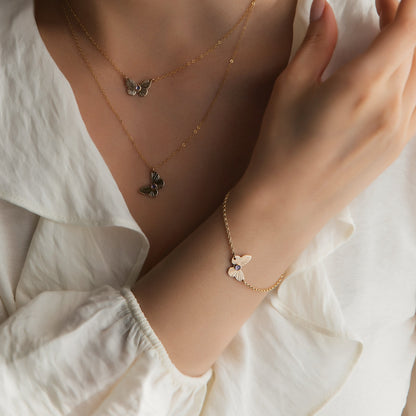 woman wearing gold butterfly necklaces and a gold butterfly bracelet wearing a white top