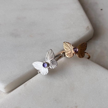 Two butterfly rings, one silver and one gold, both featuring a rose-cut tanzanite gemstone, displayed on a white surface.
