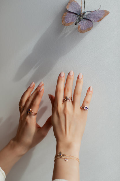 A woman wearing gold butterfly and flower rings reaching for a butterfly.