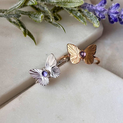 Two butterfly rings, one silver and one gold, both featuring a rose-cut tanzanite gemstone, displayed on a white surface.