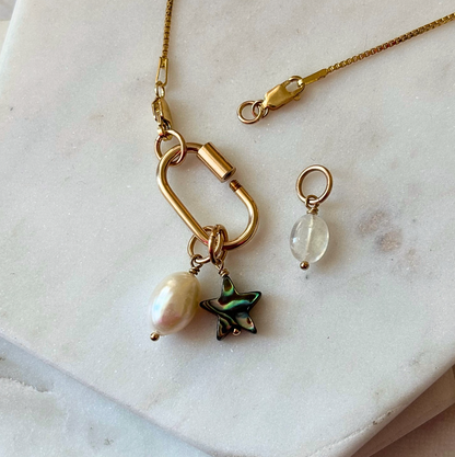 Gold necklace with star and pearl charm on a marble surface