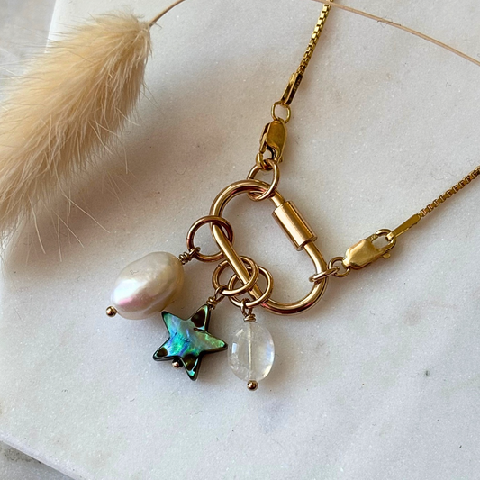 Gold necklace with a carabiner clip with star and pearl charm on a light background