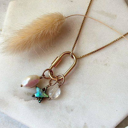 Necklace with gold clasp, pearl, and butterfly charm on a marble surface.