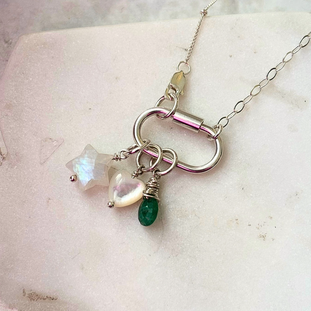 Necklace with star-shaped, heart-shaped, and teardrop-shaped gemstones on a textured surface.