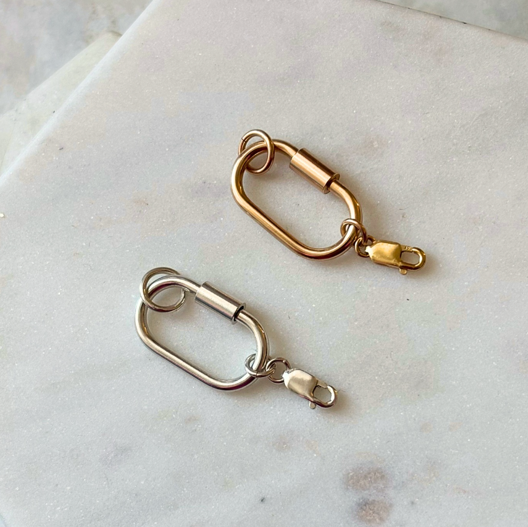 Two carabiner clips on a marble surface, one gold and one silver
