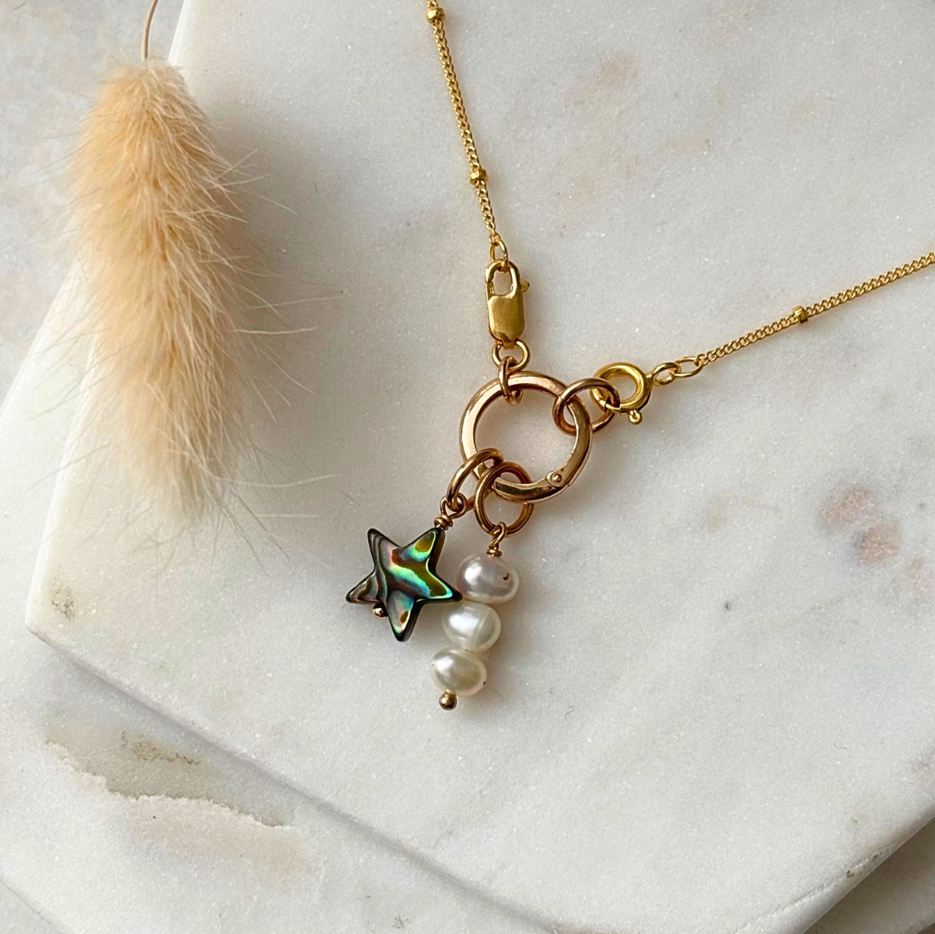 Gold necklace with star and pearl charm on a marble surface with a round charm lock