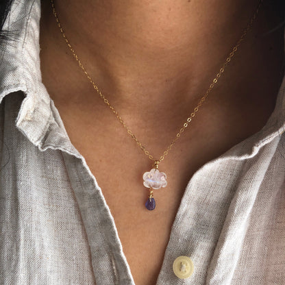 A necklace with a rainbow moonstone cloud pendant and a tanzanite raindrop, on a gold-filled chain, displayed on a person's neck.